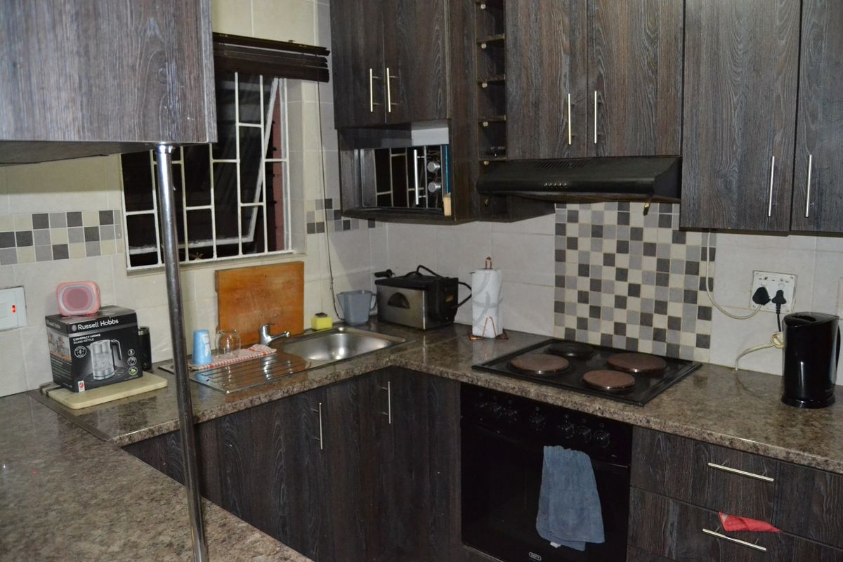 A functional kitchen featuring dark wood-look cabinetry, granite countertops, a built-in oven with electric hob, and a tiled backsplash.