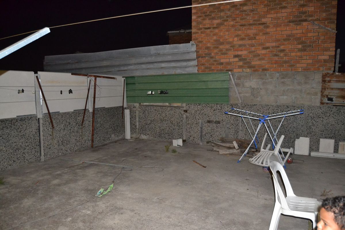 A rear outdoor area featuring concrete paving and a mix of precast concrete and corrugated metal boundary fencing.