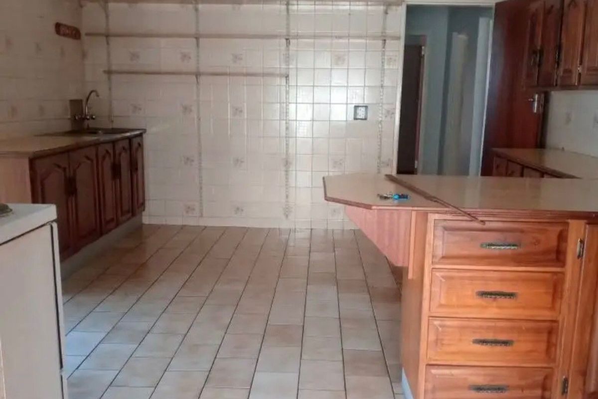 A dated kitchen featuring wooden cabinetry, tiled flooring, and wall-mounted shelving, offering a blank canvas for a modern renovation.