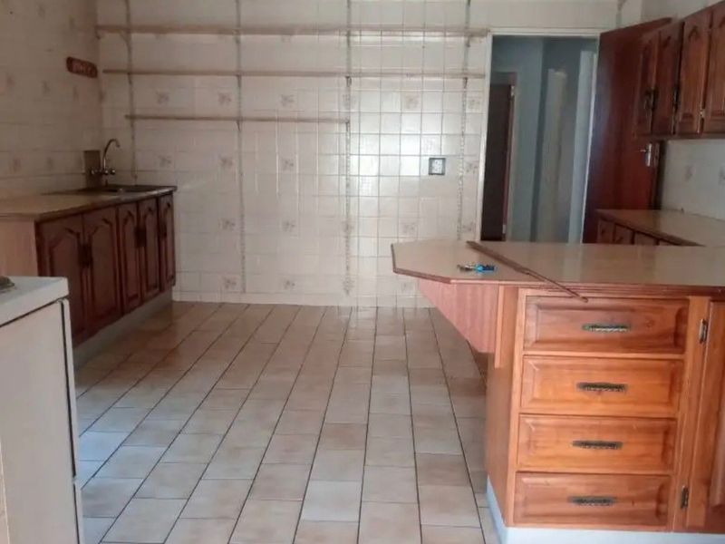 A dated kitchen featuring wooden cabinetry, tiled flooring, and wall-mounted shelving, offering a blank canvas for a modern renovation.