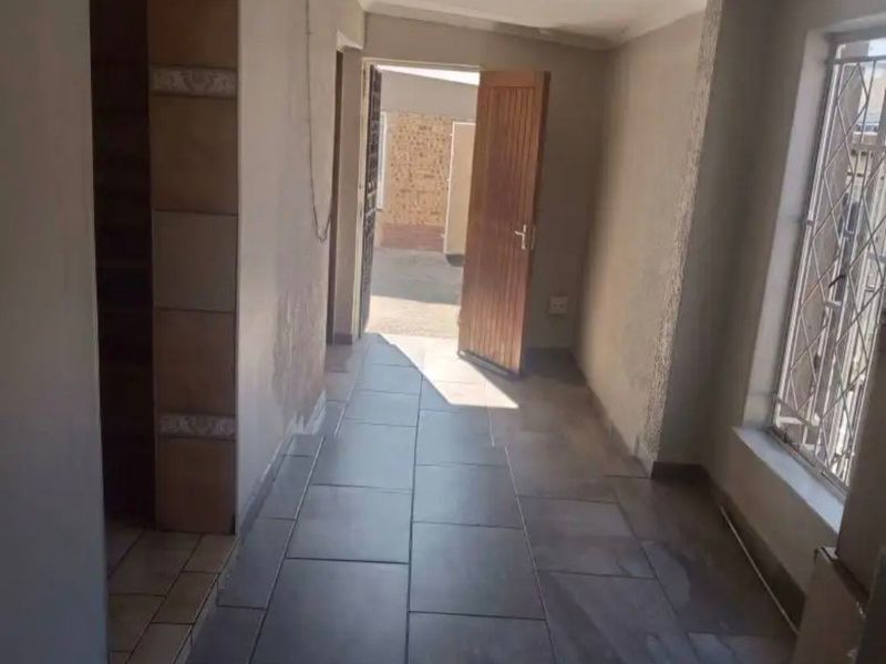 An empty hallway featuring tiled flooring, security bars on the window, and direct access to the exterior through a doorway.