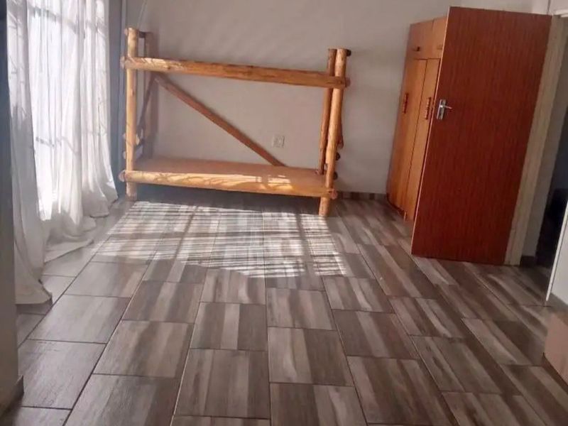 A bedroom featuring wood-look tiled flooring and natural light filtering through window curtains.