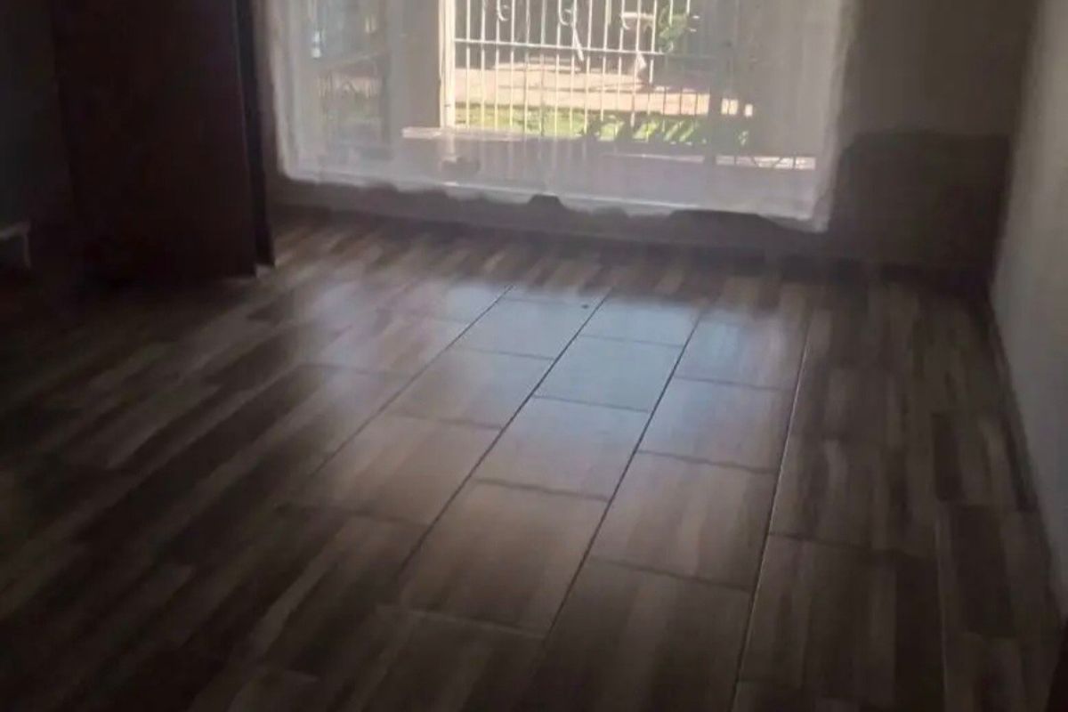 An empty bedroom featuring wood-look tile flooring and a security gate over the window, providing a blank canvas for interior design.