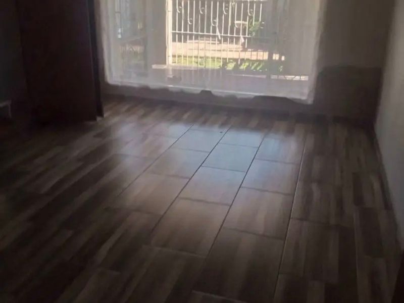 An empty bedroom featuring wood-look tile flooring and a security gate over the window, providing a blank canvas for interior design.