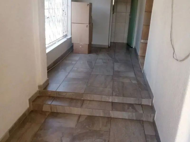 A tiled hallway featuring internal steps and security bars on the window, presenting a clean, vacant transition space within the home.