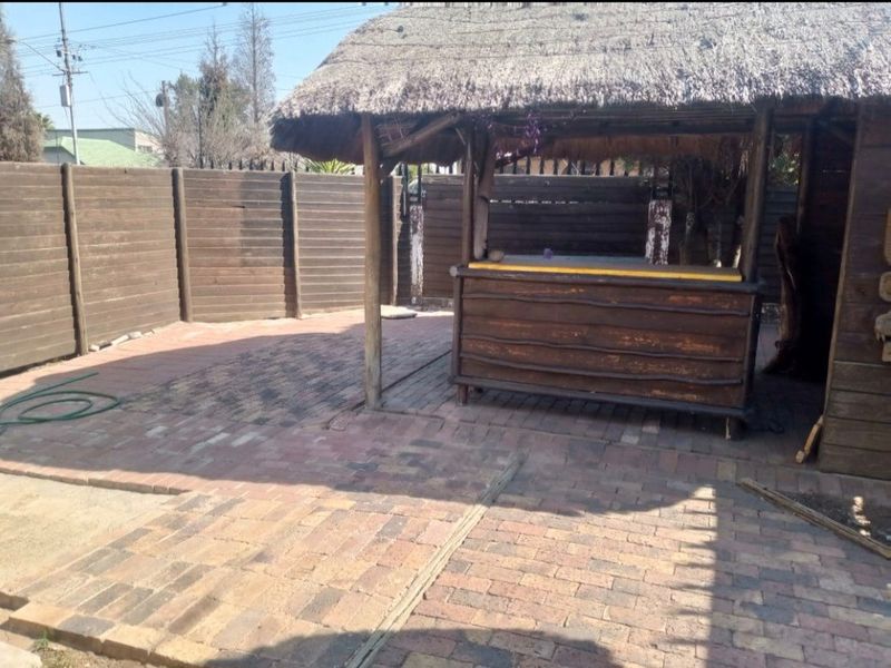 Outdoor entertainment area featuring a thatched-roof bar structure and paved patio, enclosed by timber fencing.