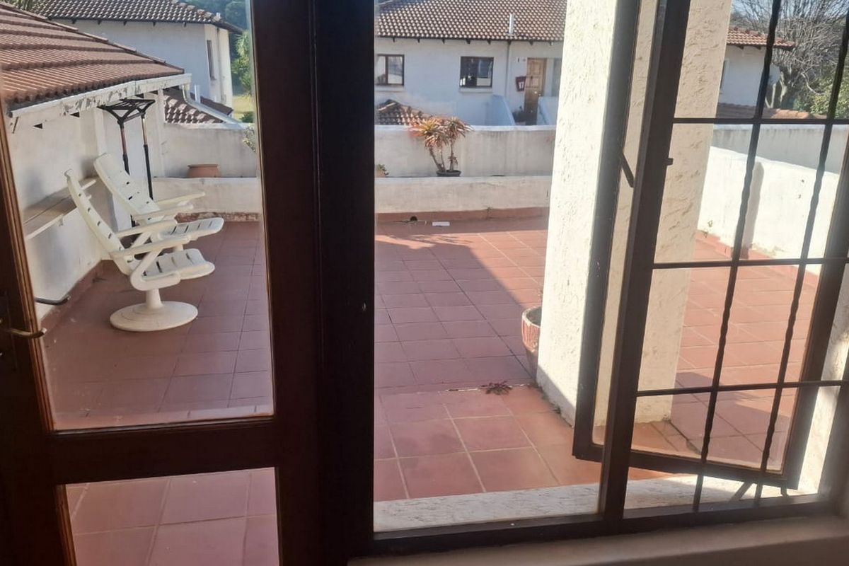 A spacious outdoor balcony featuring tiled flooring and a masonry balustrade, accessible through classic french doors, offering a functional open-air living space.