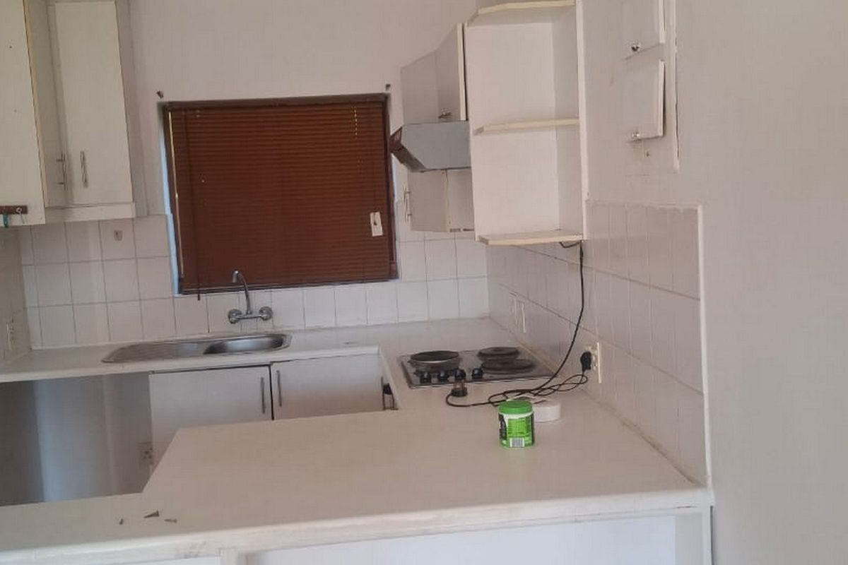 A compact, dated kitchen featuring white built-in cabinetry, a tiled backsplash, and an integrated electric hob, offering potential for a modern renovation.