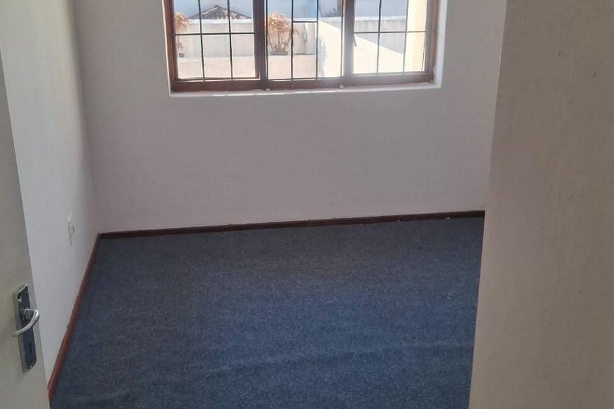 A vacant bedroom featuring carpeted flooring and a window fitted with security bars, offering a blank canvas for personalization.