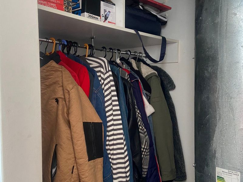 A utility closet featuring built-in shelving, a hanging rail, and an exposed water heater unit.