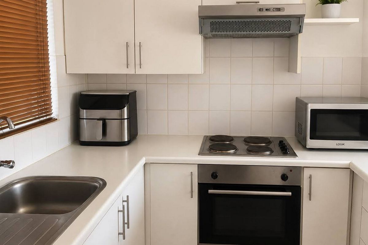 A functional kitchen featuring white cabinetry, a stainless steel sink, built-in oven with electric hob, and a tiled splashback.