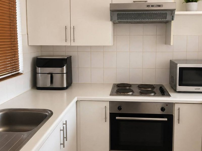 A functional kitchen featuring white cabinetry, a stainless steel sink, built-in oven with electric hob, and a tiled splashback.