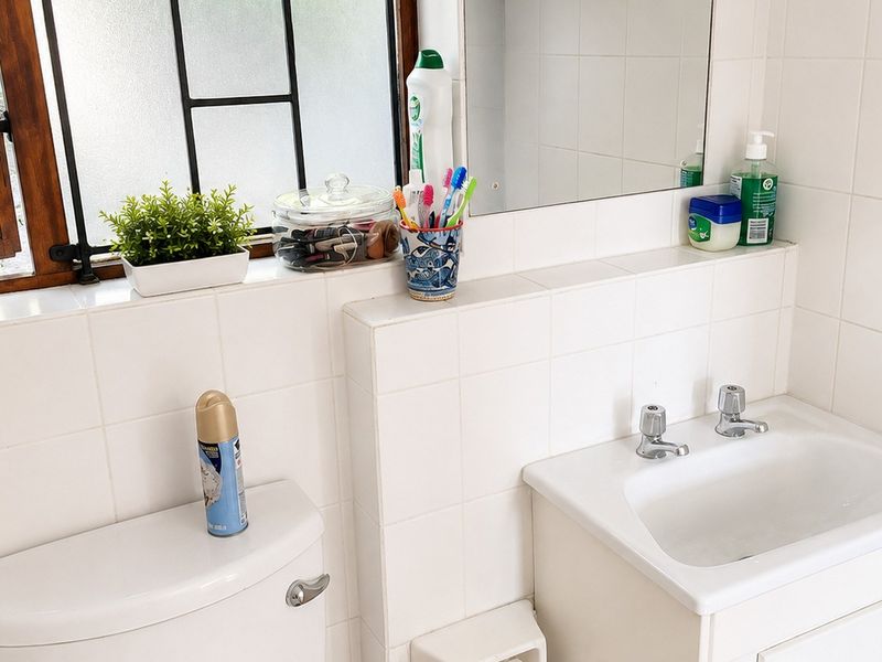A functional bathroom featuring a tiled vanity with a ceramic basin, dual tap mixer, toilet, and a window with a tiled sill.