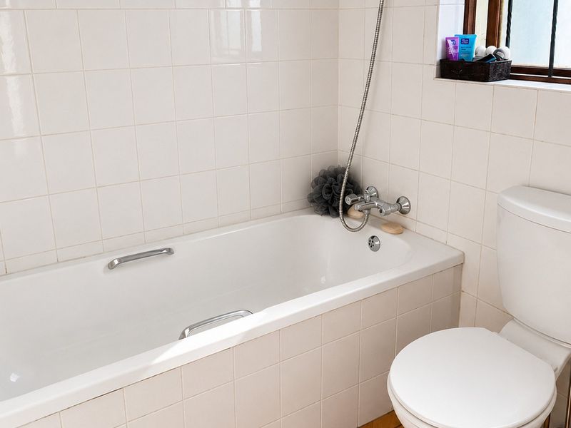 A functional bathroom featuring a standard bathtub with shower mixer, a toilet, and white wall tiling.