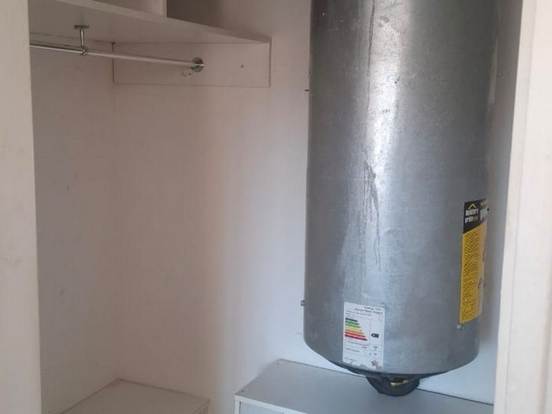 A utility cupboard housing an electric water heater with integrated shelving and a hanging rail for storage.