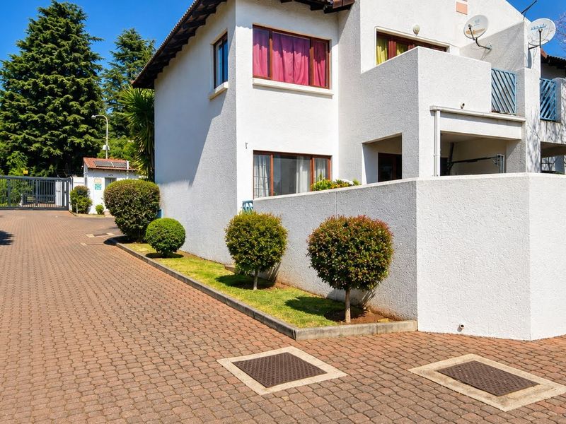 Front exterior view of a townhouse featuring a paved driveway, white facade, and a private balcony.