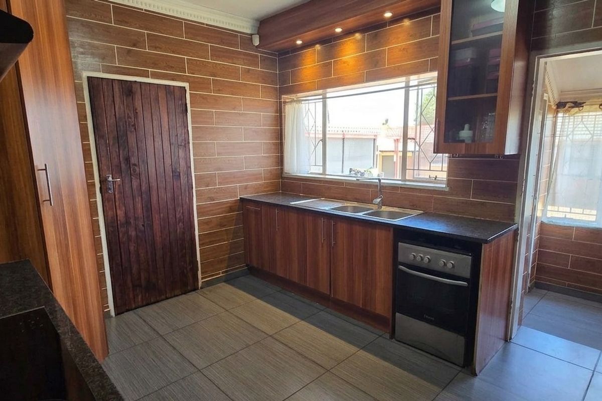A functional kitchen featuring wood-look cabinetry, tiled wall finishes, a double basin sink, and integrated lighting, providing a warm and practical cooking space.