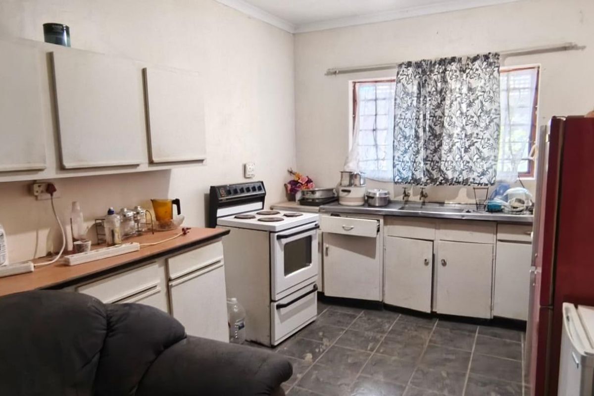 A functional kitchen featuring white cabinetry, a freestanding stove, and a double basin sink, requiring cosmetic updates to modernize the space.