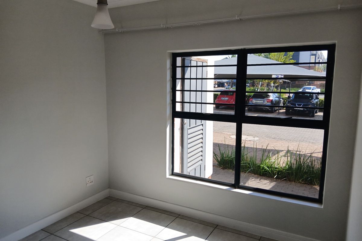 A bright, empty bedroom featuring neutral tiled flooring, a large window with security bars, and a curtain track, ready for personalization.