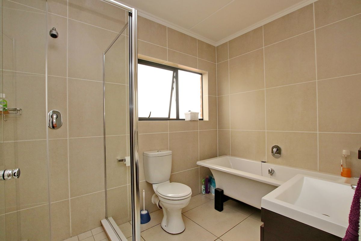 A well-maintained bathroom featuring a glass-enclosed shower, a separate bathtub, a toilet, and a vanity unit with neutral wall and floor tiling.