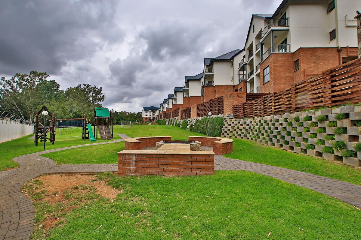 Communal garden area featuring a built-in brick fire pit, paved walkways, and playground equipment, set against the rear facade of the apartment complex.