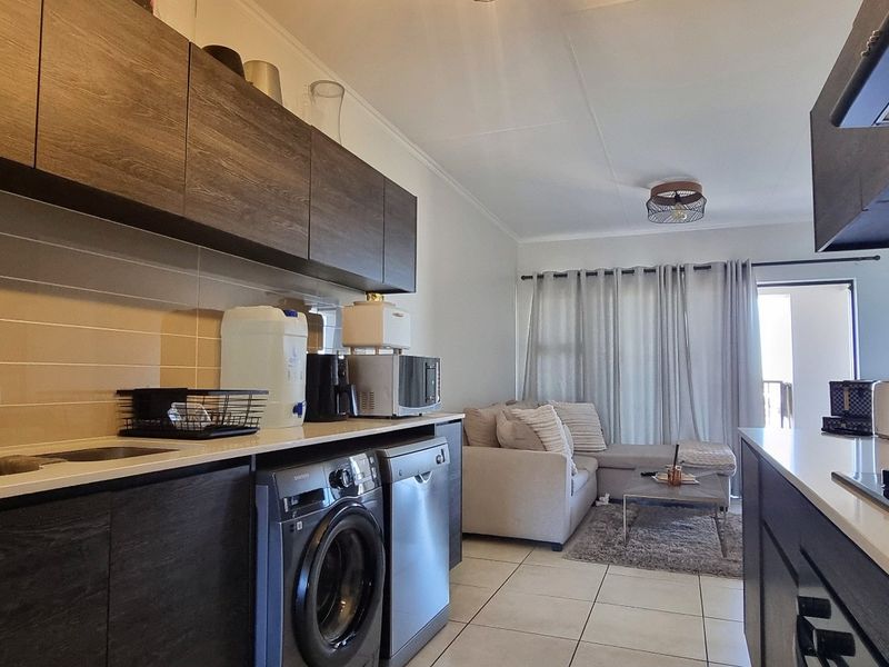 Modern open-plan kitchen and living area featuring dark wood cabinetry, stone countertops, integrated gas hob, and tiled flooring leading to a balcony.