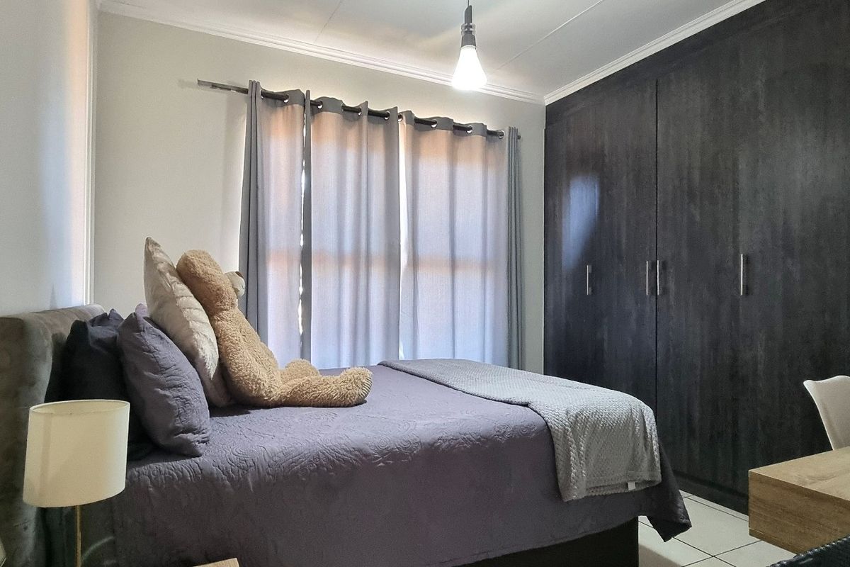 A well-maintained bedroom featuring dark wood built-in cupboards, tiled flooring, and neutral wall finishes, providing a functional and comfortable living space.