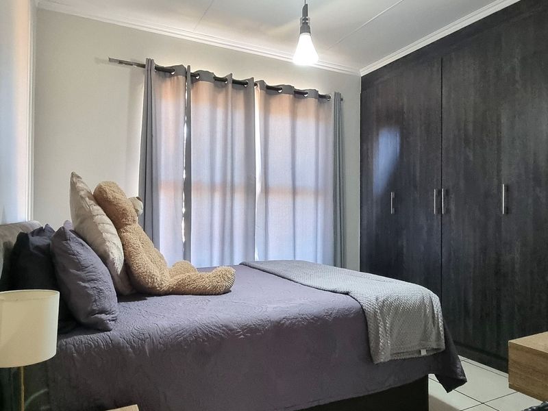 A well-maintained bedroom featuring dark wood built-in cupboards, tiled flooring, and neutral wall finishes, providing a functional and comfortable living space.