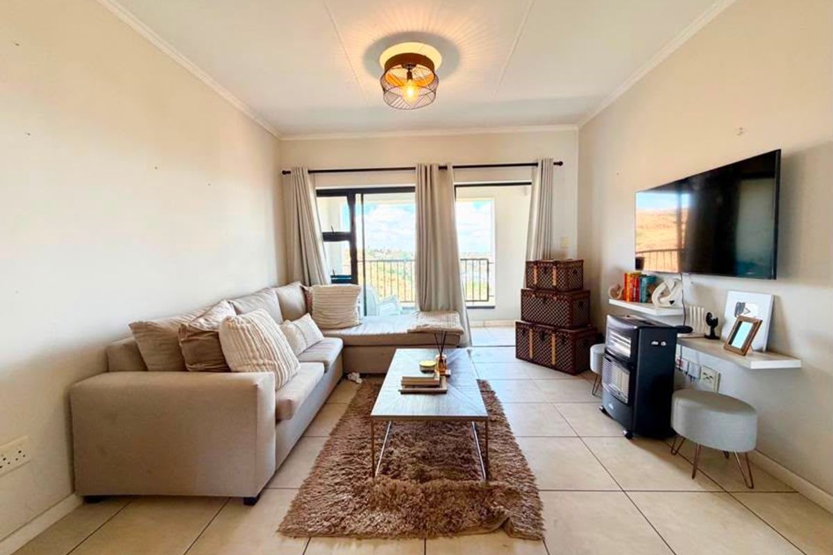 A comfortable living room featuring tiled flooring and a sliding glass door that opens onto a balcony, providing natural light and outdoor access.