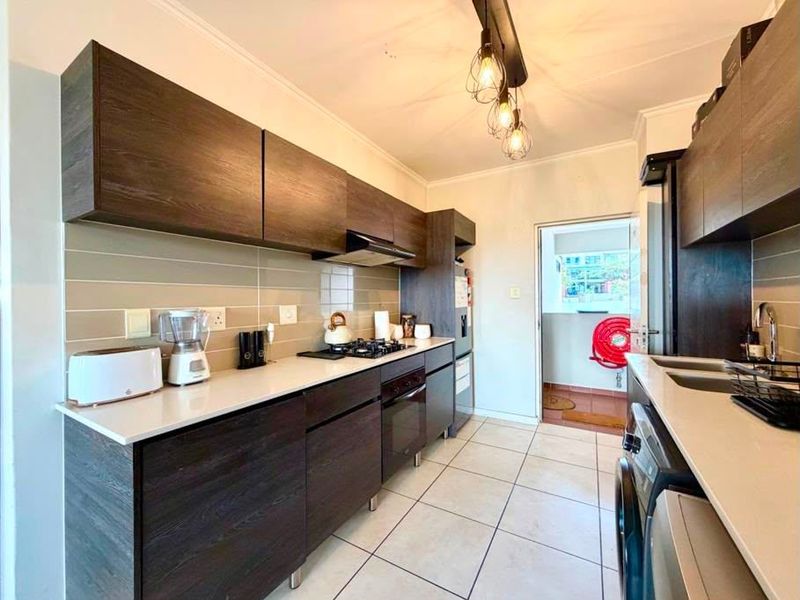 Modern kitchen featuring dark wood cabinetry, stone countertops, gas hob, built-in oven, and tiled flooring with direct access to an outdoor balcony area.
