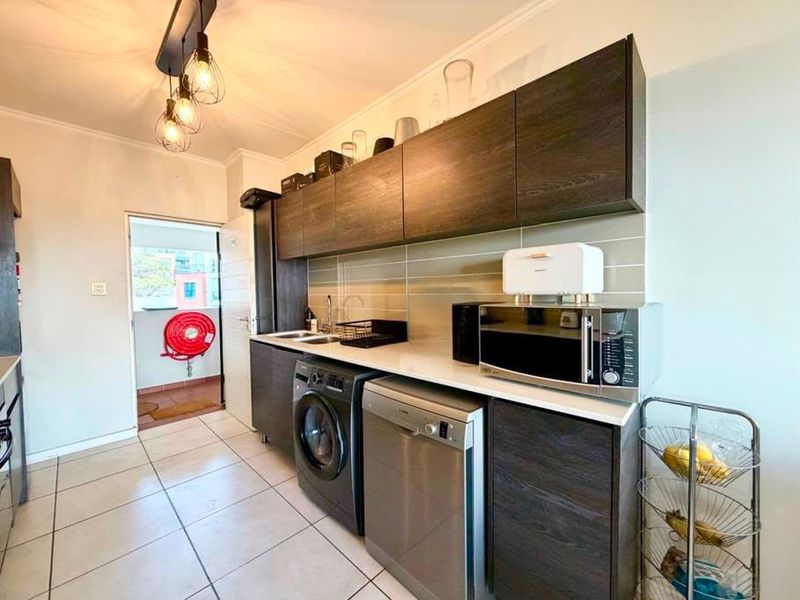 A functional scullery featuring modern dark wood cabinetry, stone countertops, tiled backsplash, and dedicated plumbing for laundry and dishwashing appliances.