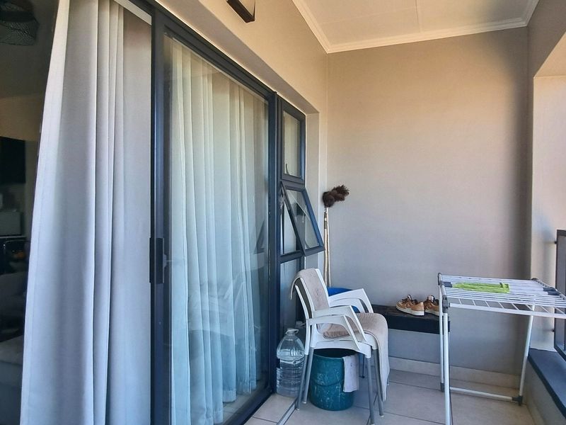 A covered balcony featuring tiled flooring and a metal balustrade, offering an outdoor space accessible through large sliding glass doors.