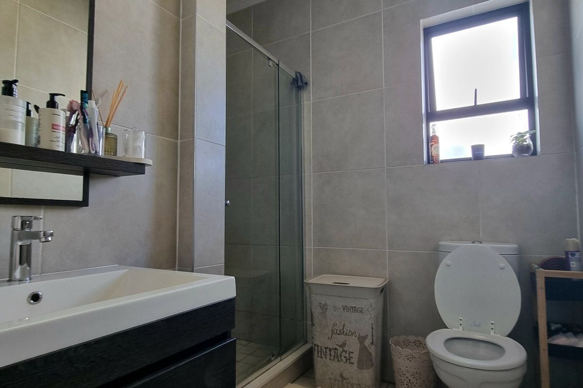 A modern bathroom featuring a vanity with basin, a glass-enclosed shower, and neutral ceramic wall tiling.