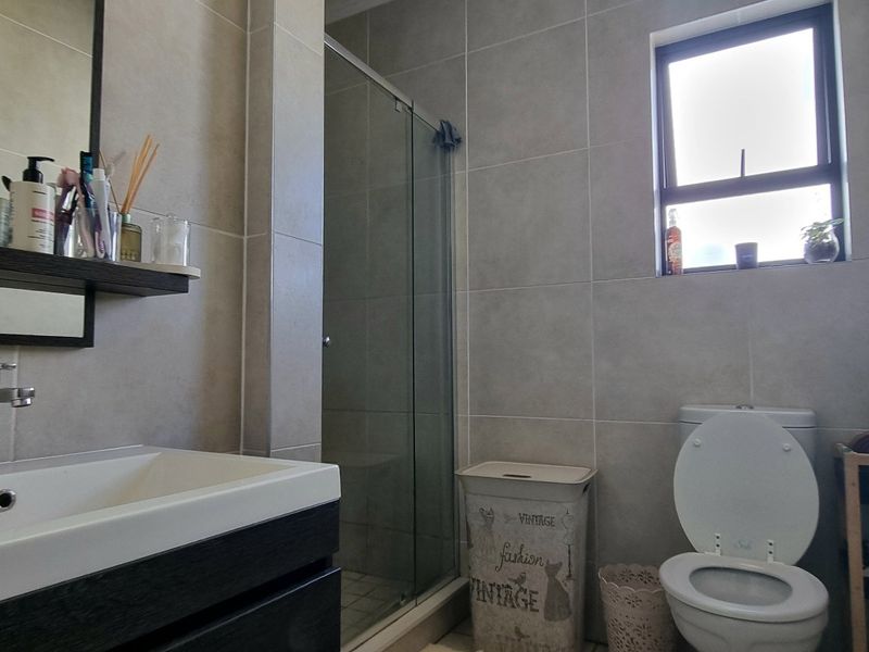 A modern bathroom featuring a vanity with basin, a glass-enclosed shower, and neutral ceramic wall tiling.