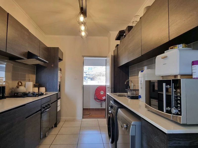 Modern galley-style kitchen featuring dark wood-grain cabinetry, stone countertops, gas hob, built-in oven, and tiled flooring with direct access to a balcony.