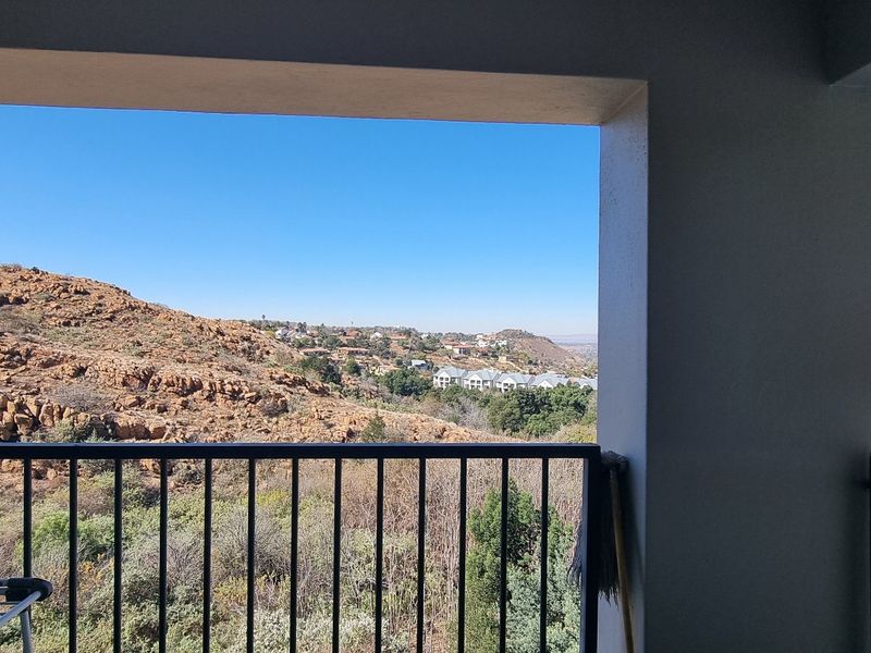 A covered balcony featuring a metal balustrade and expansive views of the surrounding rocky landscape and residential area.
