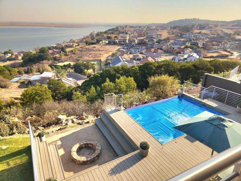 Elevated outdoor pool area featuring a modern deck, stone fire pit, and stainless steel balustrades with expansive views of the surrounding landscape and water.