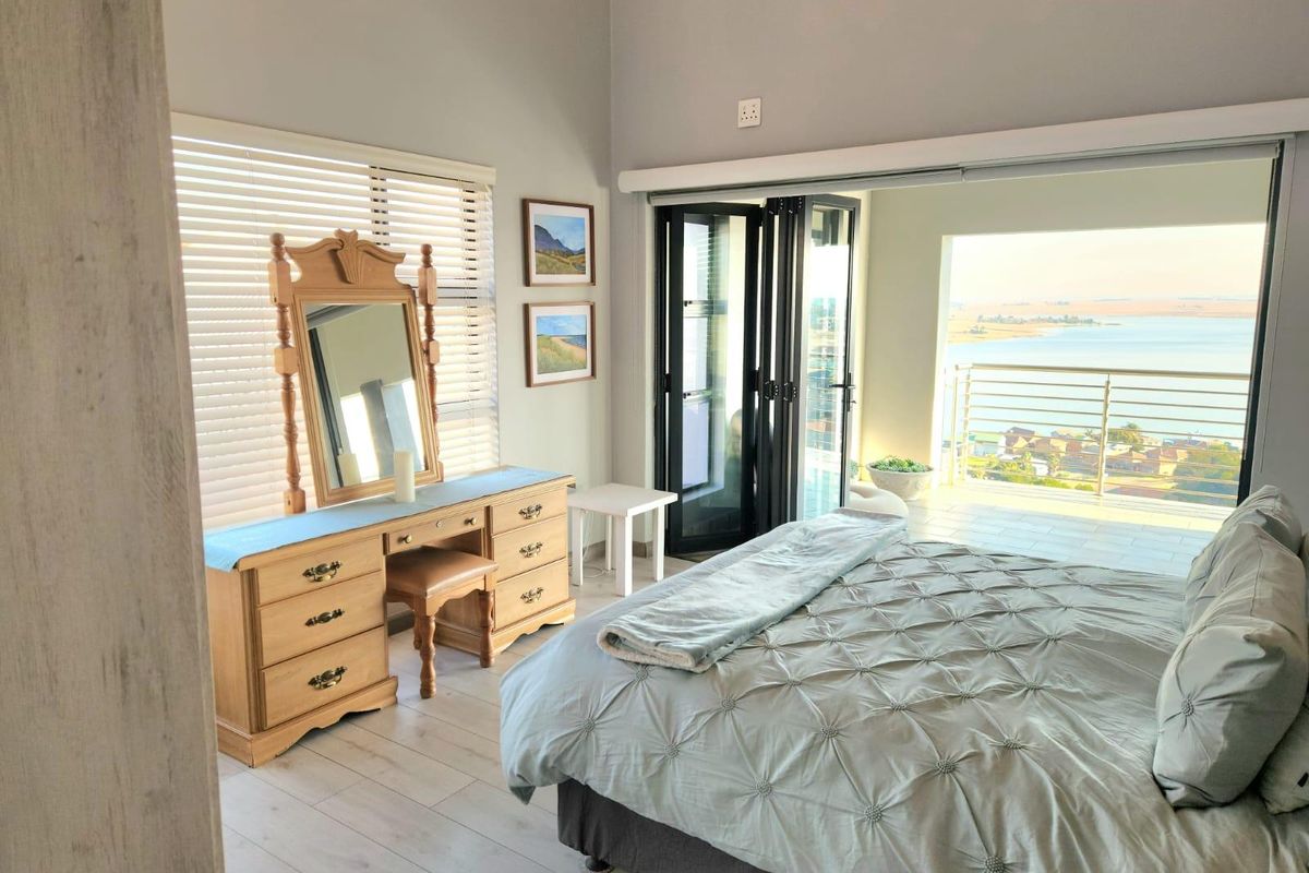 Spacious bedroom featuring light laminate flooring, venetian blinds, and large bi-fold doors opening onto a balcony with scenic water views.