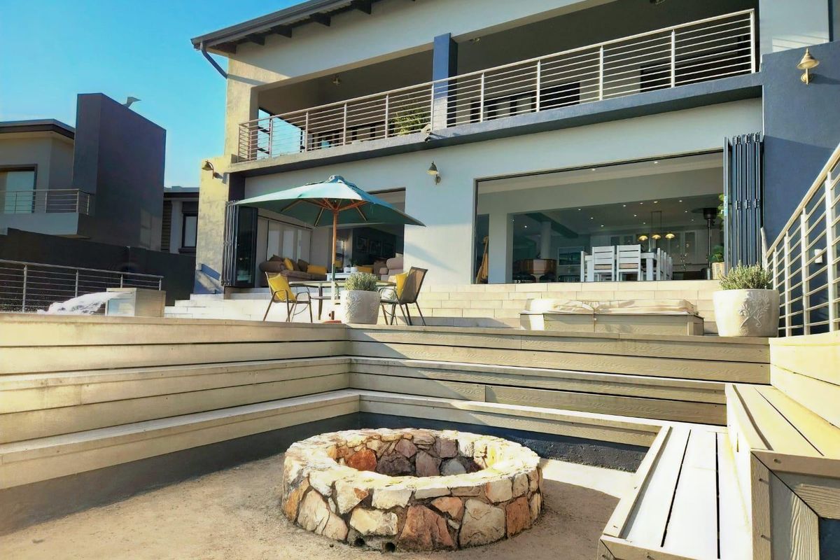 Rear exterior view featuring a tiered timber deck, stone fire pit, and a spacious balcony overlooking the outdoor entertainment area.