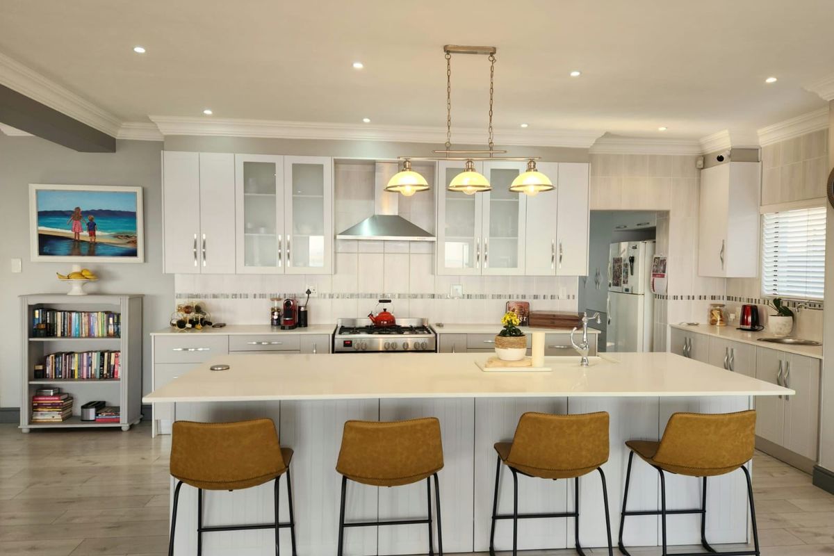 Modern kitchen featuring a large central island with quartz countertops, gas cooktop, stainless steel extractor fan, and ample white cabinetry.