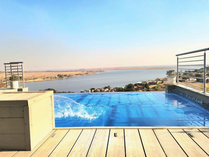 An infinity edge swimming pool featuring timber decking and stainless steel balustrades, offering expansive views over the lake and surrounding landscape.
