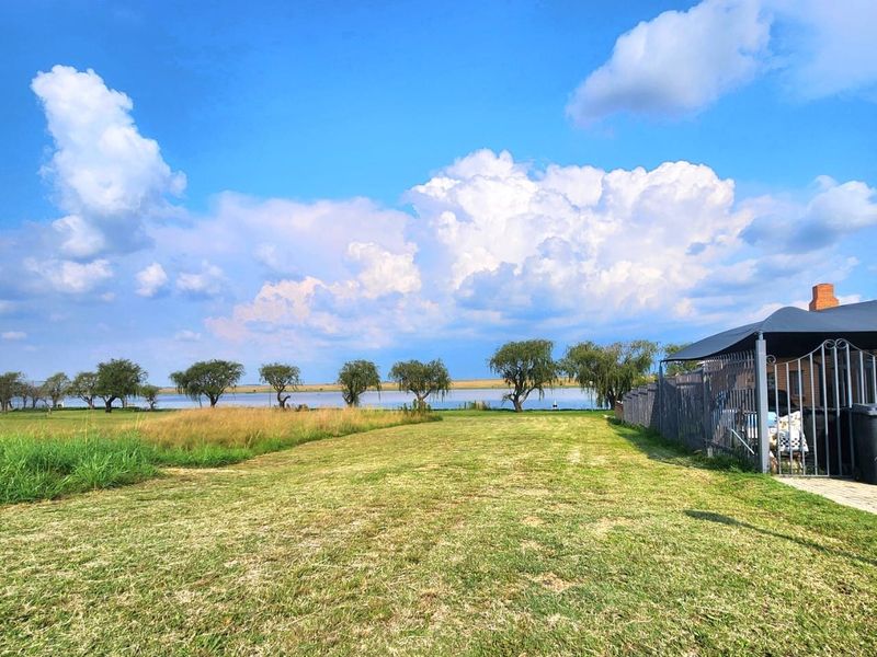 A spacious residential lawn area featuring perimeter fencing and a view of the adjacent water body and landscape.