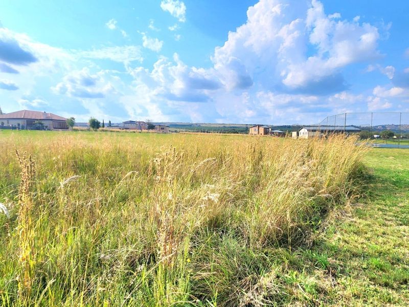 A wide-angle view of an expansive, undeveloped residential plot featuring natural grassland and surrounding neighborhood views.