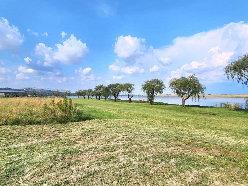 A scenic view of a waterfront property featuring expansive green lawns and mature trees along the shoreline.