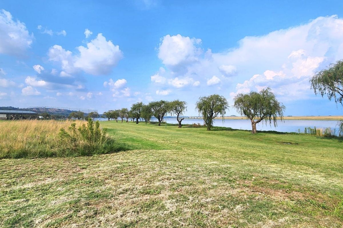 A scenic view of a waterfront property featuring expansive green lawns and mature trees along the shoreline.