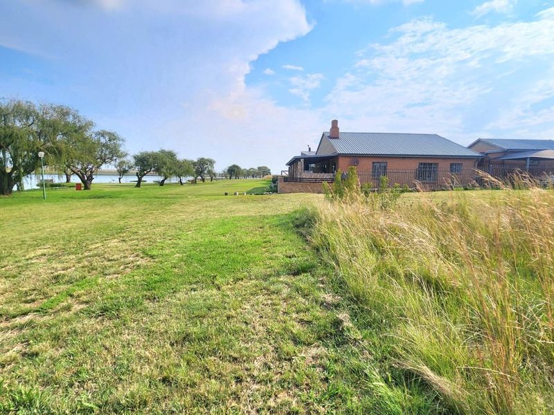 A view of the rear exterior of a brick residential property featuring a metal roof, chimney, and expansive lawn area overlooking a water feature.