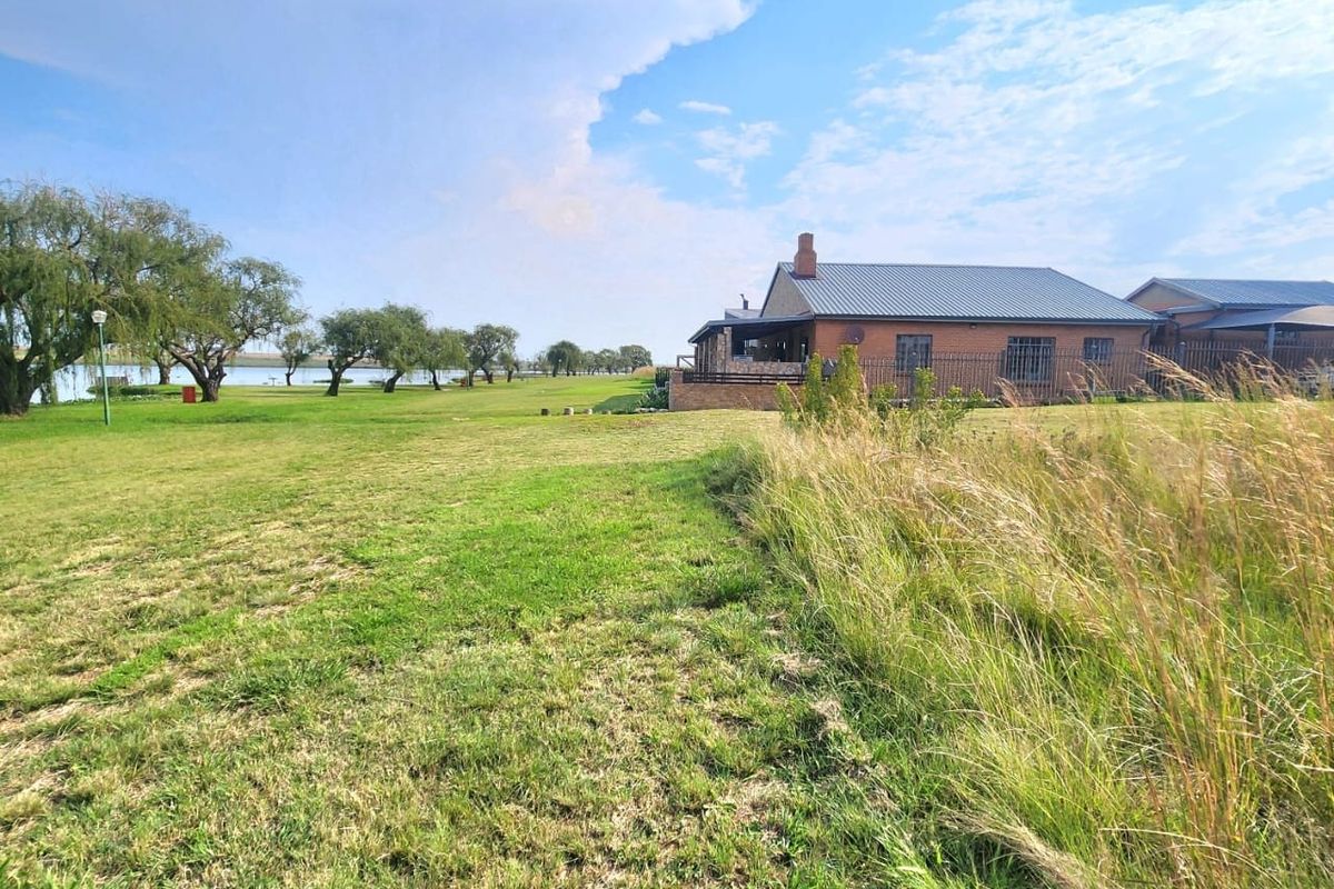 A view of the rear exterior of a brick residential property featuring a metal roof, chimney, and expansive lawn area overlooking a water feature.