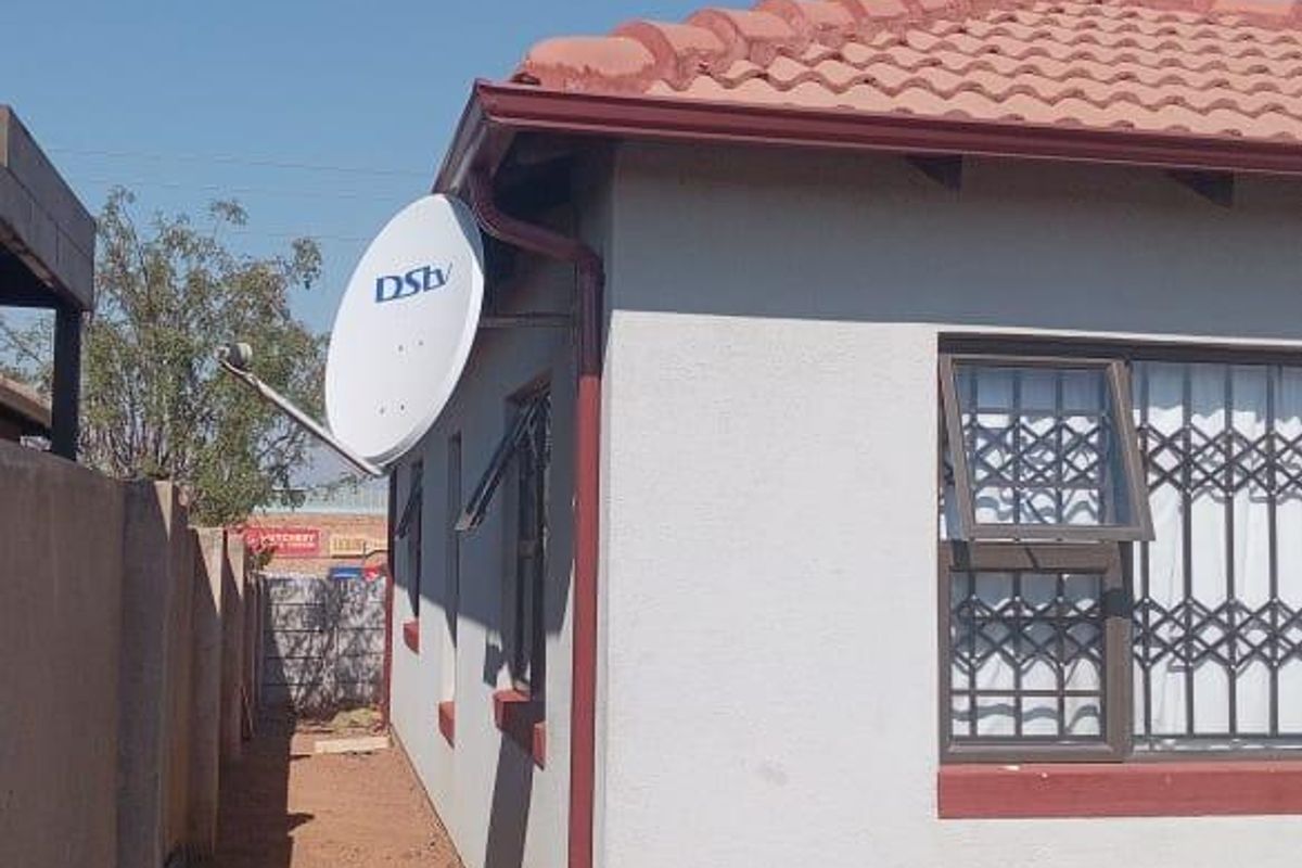 Side view of the property showing the exterior wall, tiled roof, security bars on windows, and a satellite dish installation.