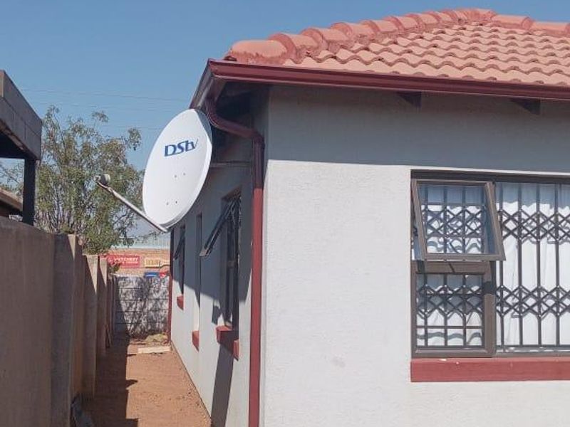 Side view of the property showing the exterior wall, tiled roof, security bars on windows, and a satellite dish installation.