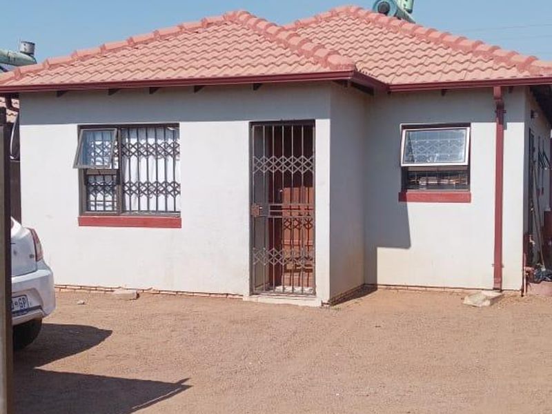 Front elevation of a single-story house featuring a tiled roof, security gates, burglar bars, and an installed solar geyser system.